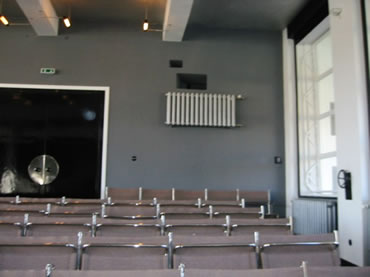 Audimax, Farvspill mit warmfarvde Sitze v&ouml;r dei farvig tr&uuml;ggaohn Achterwand g&auml;gen dei lechten Fensterfront